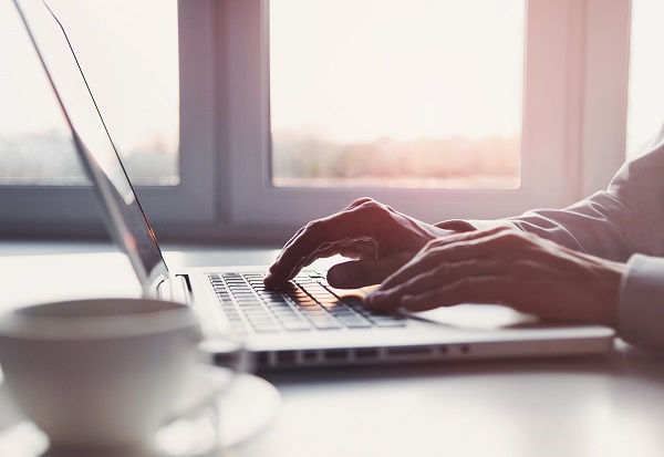 Imagen de manos de hombre escribiendo en el teclado de un computador portátil