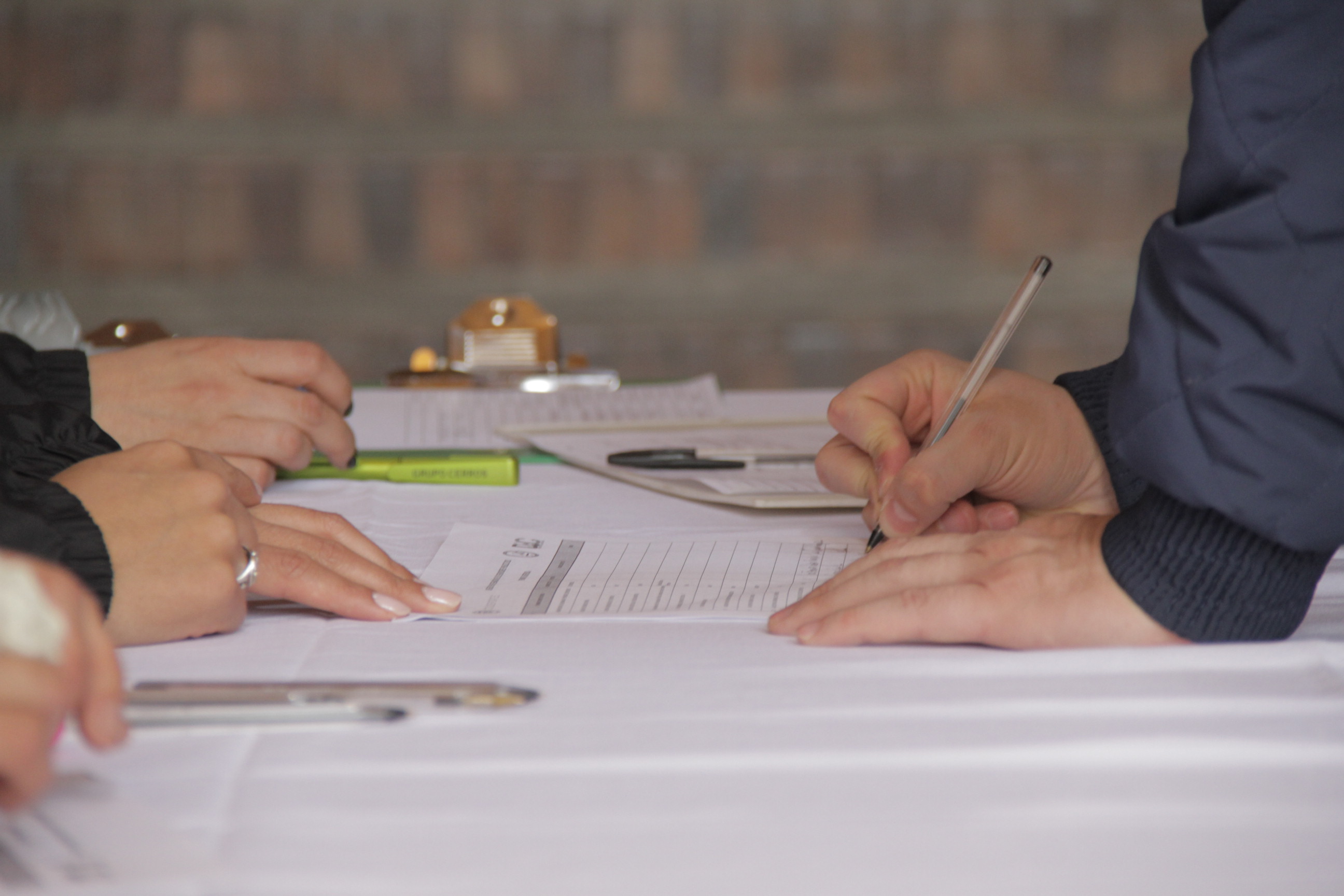 Imagen de manos sobre una mesa, y alguien escribiendo en un papel.