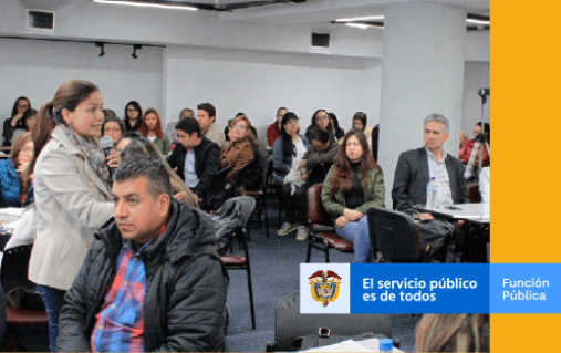 Mujer con micrófono en mano hablando en medio de personas en un auditorio