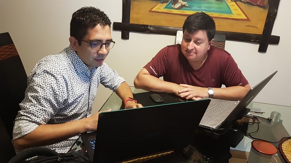 Dos hombre sentados en el comedor mirando una pantalla de computador 