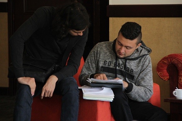 Dos jóvenes sentados en una silla mirando unos papeles