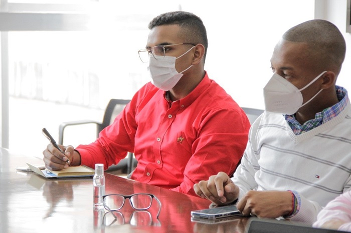 Dos hombres jóvenes afrodescendientes con tapabocas sentados frente a una mesa tomando apuntes