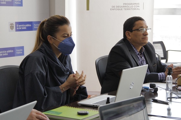 Un hombre y una mujer con tapabocas sentados en una mesa de conferencias