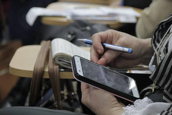 Manos de mujer con un teléfono celular y un esfero en cada una