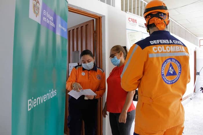 Dos mujeres y un hombre, de pie junto a una puerta. El hombre lleva puesto el uniforme de la Defensa Civil