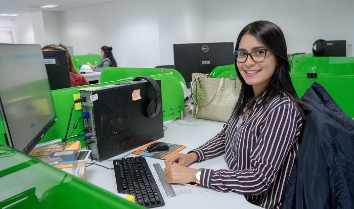 Mujes sonriente mirando a la cámara y sentada en un puesto de trabajo en una oficina