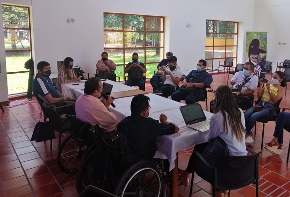 Personas reunidas en un salón a lo largo de una mesa. Algunos están sentados en sillas de ruedas.