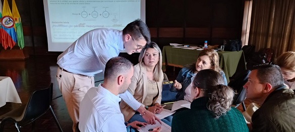 Varias personas en una oficina, un servidor pública los orienta sobre algún tema.