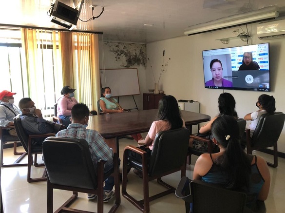 Mujeres y hombres sentados alrededor de una mesa ovalada y mirando a una pantalla grande televisión