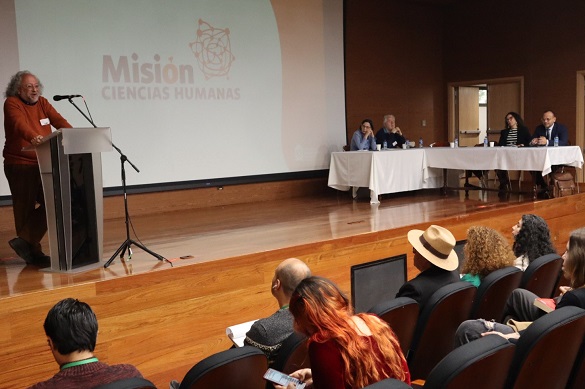 Un hombre en un atril sobre una tarima, hablando ante un auditorio