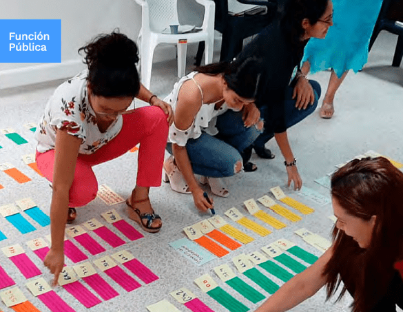 Cuatro mujeres jóvenes acurrucadas mirando papeles de colores que se encuentran pegados en el piso