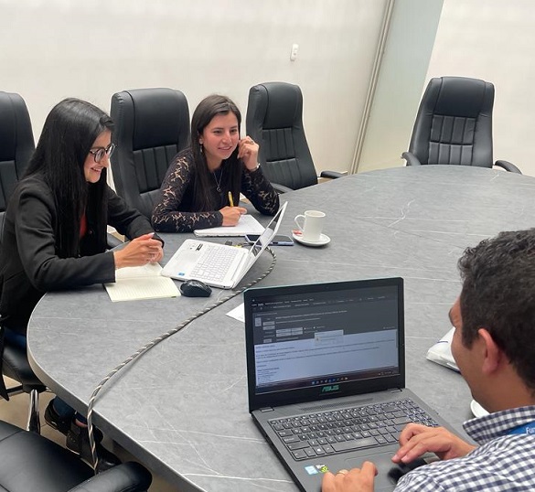 Dos mujeres jóvenes sentadas frente a un hombre joven con un computador portátil