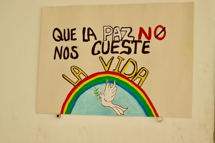 Dibujo de un carte en donde se ve unapaloma de la paz con un arcoiris y el texto Que la paz no nos cueste la vida
