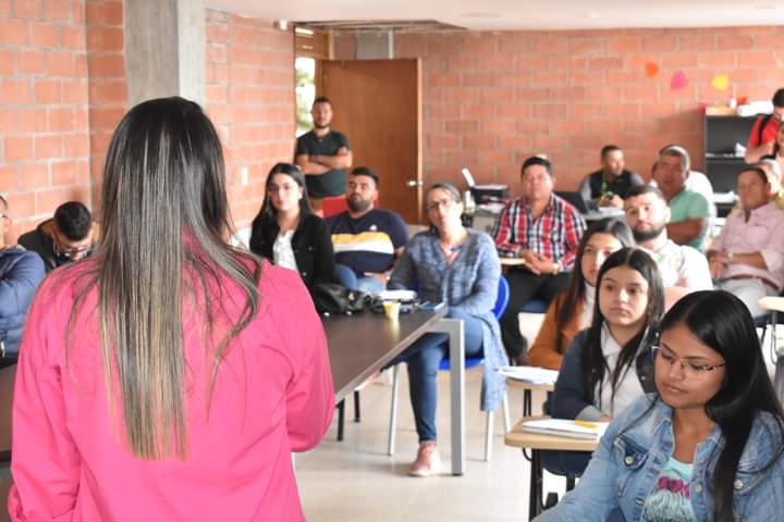 Una mujer se dirige a un grupo de personas en un salón de clases 