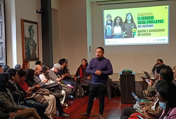 Grupo de personas sentadas al rededor de un hombre que está en el centro de pie, exponiendo un tema