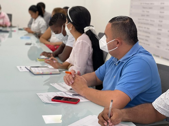 Grupo de personas con tapabocas sentadas en torno a una mesa de juntas